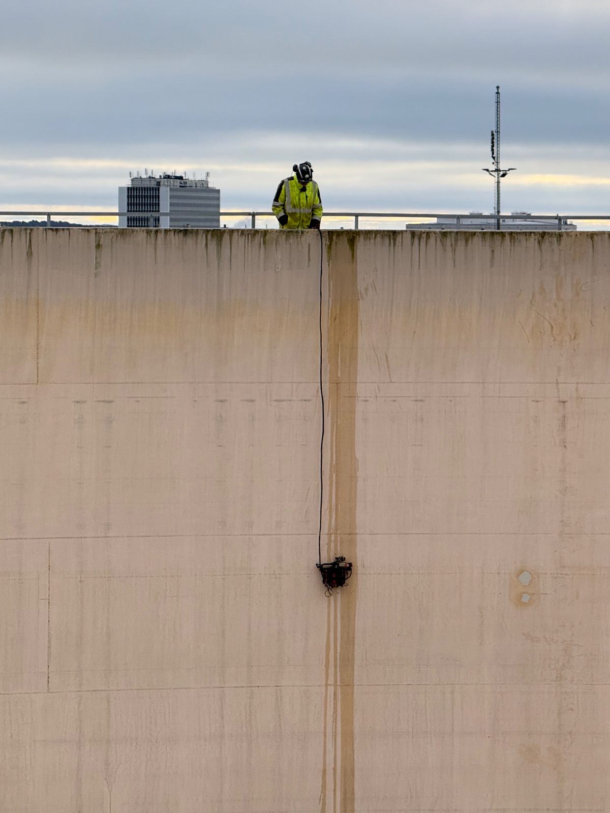 Inspector on the tank rim with a scanning crawler on the shell wall